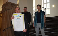 Oberbürgermeister Andreas Mucke mit der Urkunde, hinter ihm Susanne Varnhorst und Dezernent Frank Meyer