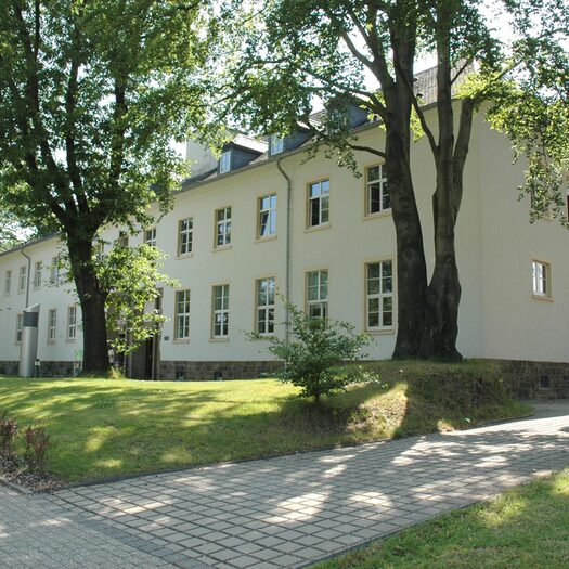 Campus Freudenberg, großes weißes Gebäude mit Bäumen und Rasen im Vordergrund