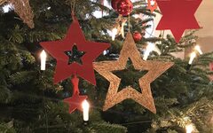 Nahaufnahme eines geschmückten Weihnachtsbaumes mit goldenen und roten Sternen und Lichterkette