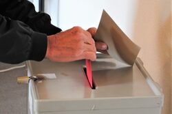 Ein Briefwahlumschlag wird im rathaus in eine Wahlurne gesteckt