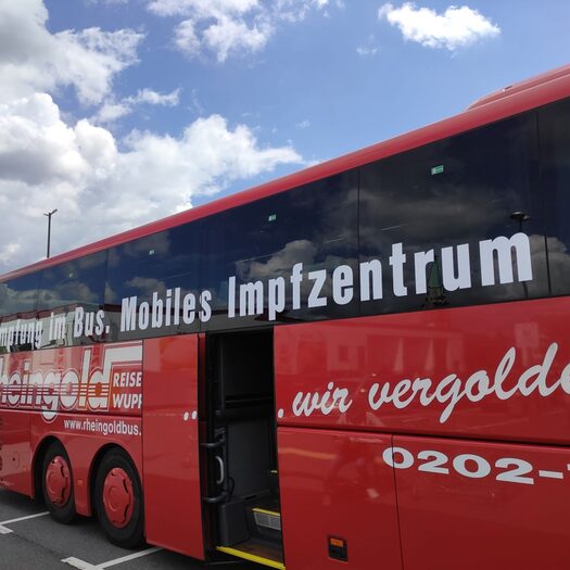Ein roter Bus mit der Aufschrift "Mobiles Impfzentrum" vor blauem Himmel mit weißen Wolken