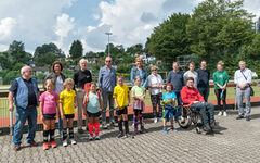 Kinder aus den Feriensportkursen mit den Mitgliedern des Sportausschusses und Vertretern des Sport- und Bäderamtes vor einem Sportplatz