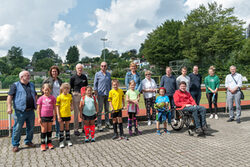Kinder aus den Feriensportkursen mit den Mitgliedern des Sportausschusses und Vertretern des Sport- und Bäderamtes vor einem Sportplatz