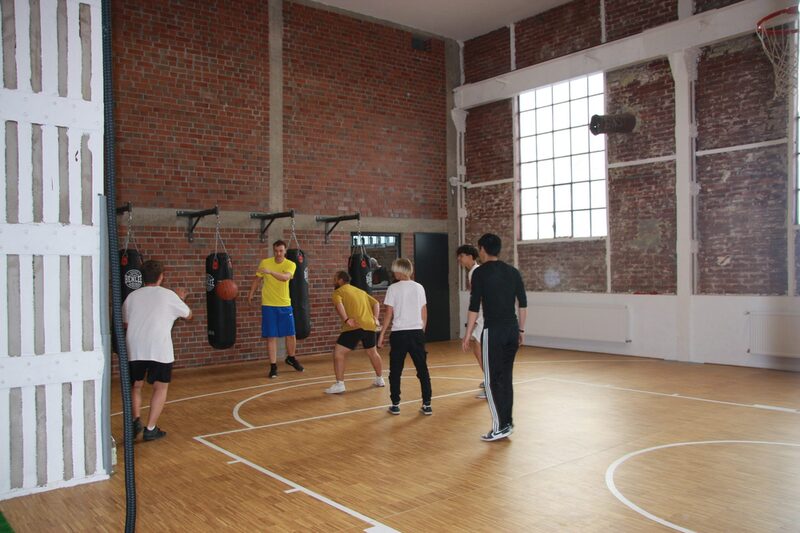 Jugendliche beim Basketballtraining in einer Halle mit roten Backsteinwänden