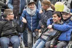Kinder in blauen Anoraks sitzen im Rollstuhl oder stehen daneben