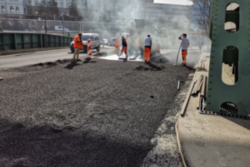 Arbeiter tragen auf der Islandbrück einen neuen Straßenbelag auf