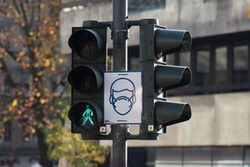 In der Innenstadt weisen Schilder auf die Maskenpflicht hin - hier ein Schild an einer grünen Fußgängerampfel