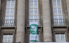 Die Fahne mit einer weißen Friedenstaube vor grünem Grund an der Fassade des Rathauses