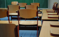 Blick in ein Klassenzimmer mit Tafel und hochgestellten Stühlen auf Tischen