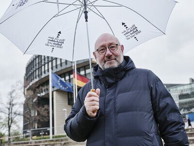 Stadtdirektor und Kämmerer Dr. Slawig mit einem weißen Regenschirm und dem Slogan des Aktionsbündnisses