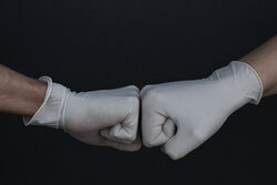 zwei Hände in Einmalhandschuhen begrüßen sich per Faustgruß