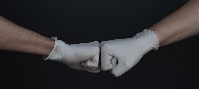 zwei Hände in Einmalhandschuhen treffen sich zum Faustgruß