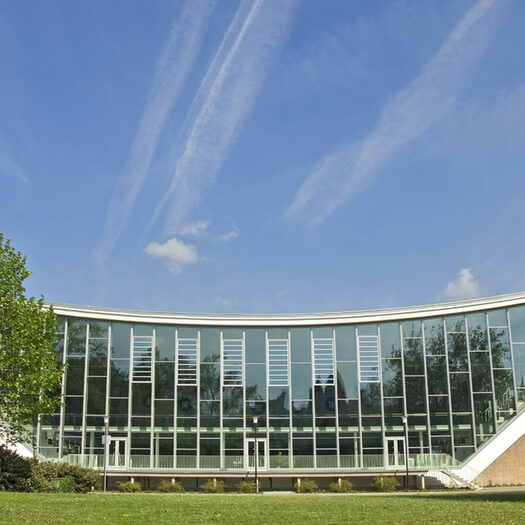 Außenansicht der Schwimmoper mit Glasfassade vor blauem Himmel