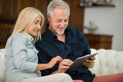 Älteres Ehepaar sitzt auf dem Sofa und schaut gemeinsam auf ein Tablet