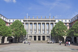 Rathausgebäude mit Seitenflügeln und Platz mit Bäumen im Vordergrund