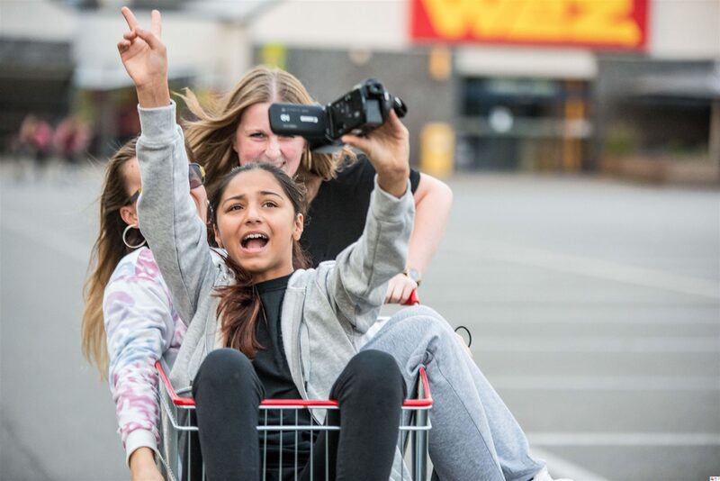 Mädchen sitzen in einem Einkaufswagen und halten eine Kamera in der Hand
