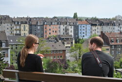 Zwei Menschen sitzen auf einer Bank, im Hintergrund eine Oberbarmer Häuserzeile