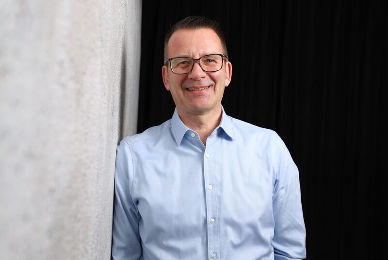Portrait Stadtkämmerer Thorsten Bunte mit hellblauem Hemd vor dunklem Hintergrund