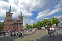 Laurentiusplatz mit Kirche im Hintergrund. Das sommerliche Motiv zeigt Passanten und Nutzer des Platzes.