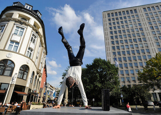 Skulptur eines Mannes, der Handstand macht, im Hintergrund Gebäude und Fußgängerzone