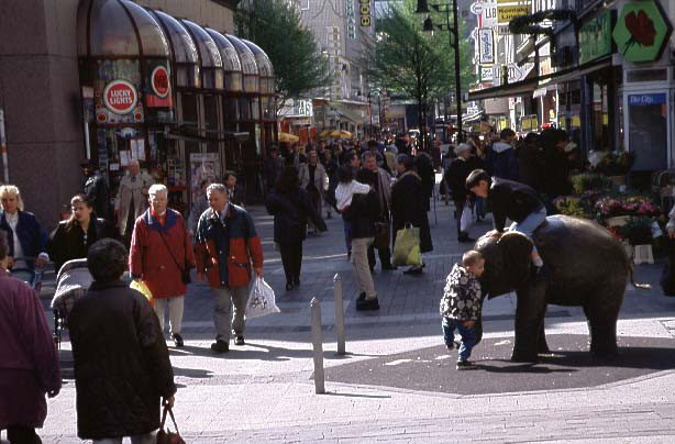 Passanten in der Fußgängerzone, Arkaden, Geschäfte und Bäume