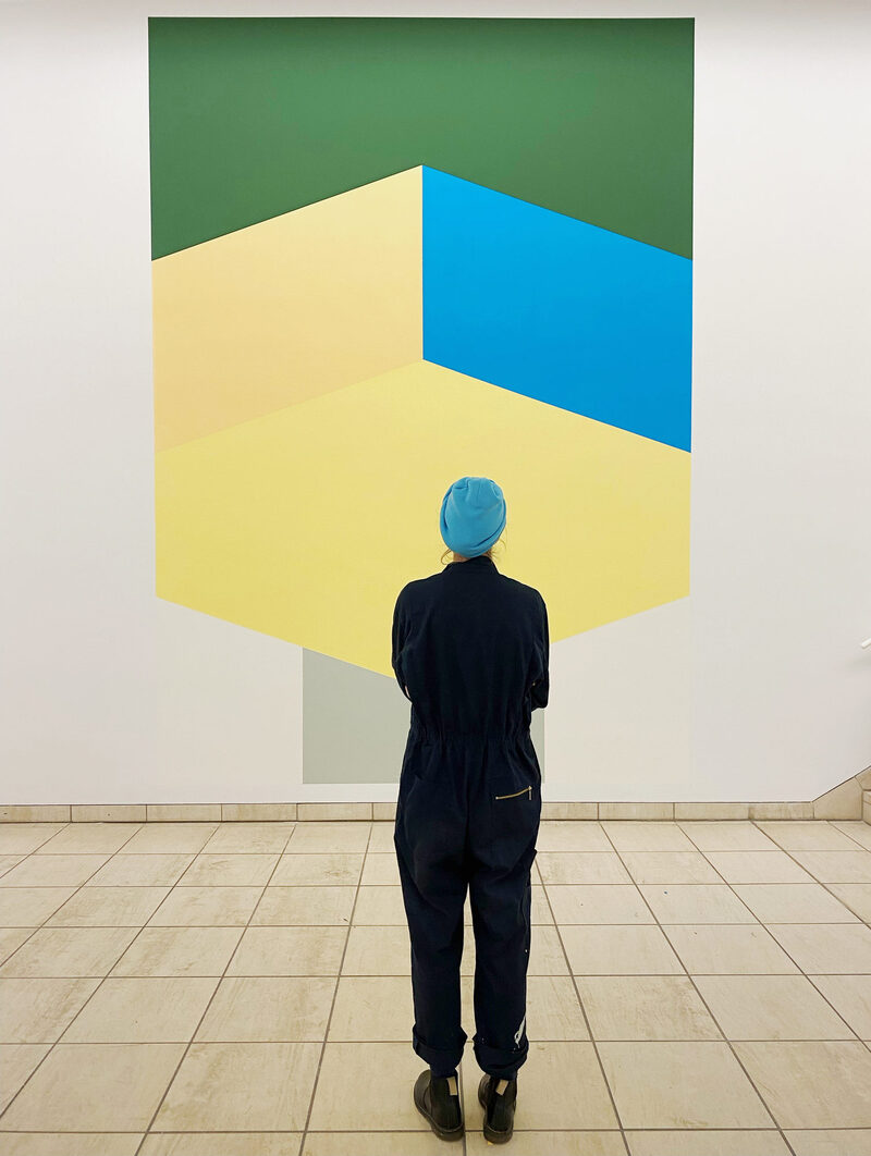 Die Künsterlerin Franziska Holstein, von hinten zu sehen, betrachtet ihr Bild in klaren geometrischen Formen und den Farben gelb, grün und blau im Von der Heydt-Museum