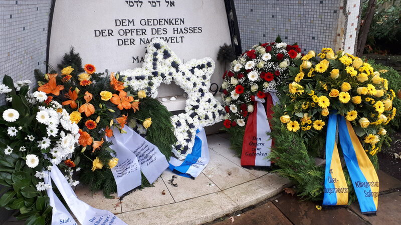 Kränze mit bunten Blumen liegen vor einer Gedenktafel für "die Opfer des Hasses" (Inschrift)