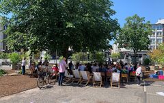Gottesdienst unter freiem Himmel auf dem Platz am Kolk. Menschen sitzen auf Stühlen unter einem Baum.