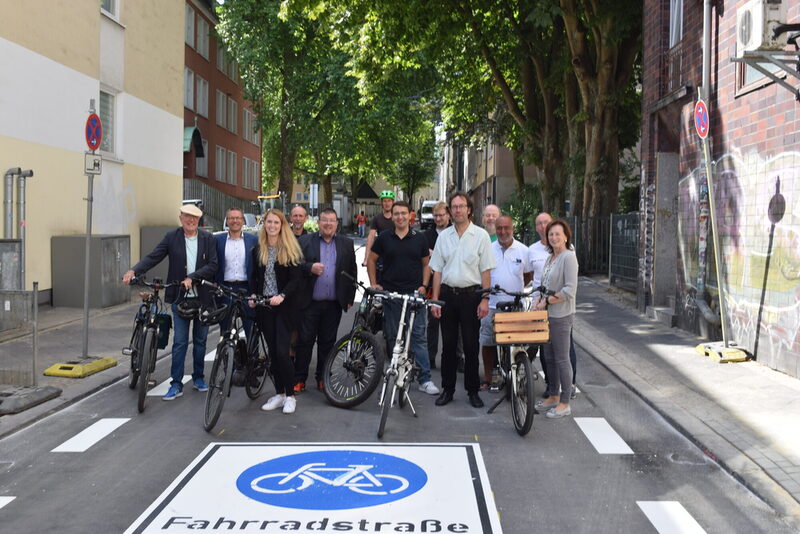 Eine Personengruppe mit Fahrrädern steht vor einem Piktogramm Fahrradstraße