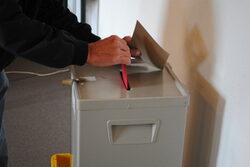 Person steckt einen Wahlzettel in die Wahlurne