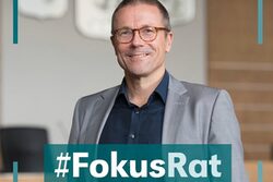OB Uwe Schneidewind lächelt in die Kamera. Aufnahme im Ratssaal. Im unteren Bildbereich der Schriftzug "#FokusRat".
