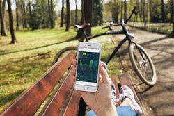 Eine Hand hält ein Handy, im Hintergrund stehe ein Fahrrad