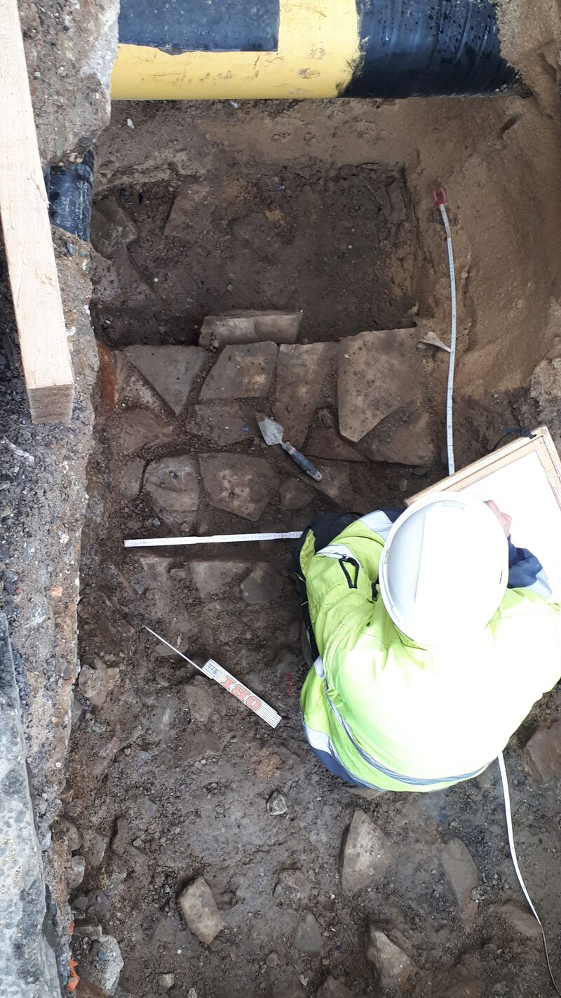 Burgmauerreste in einer Baugrube, Archäologe mit Helm und gelber Jacke