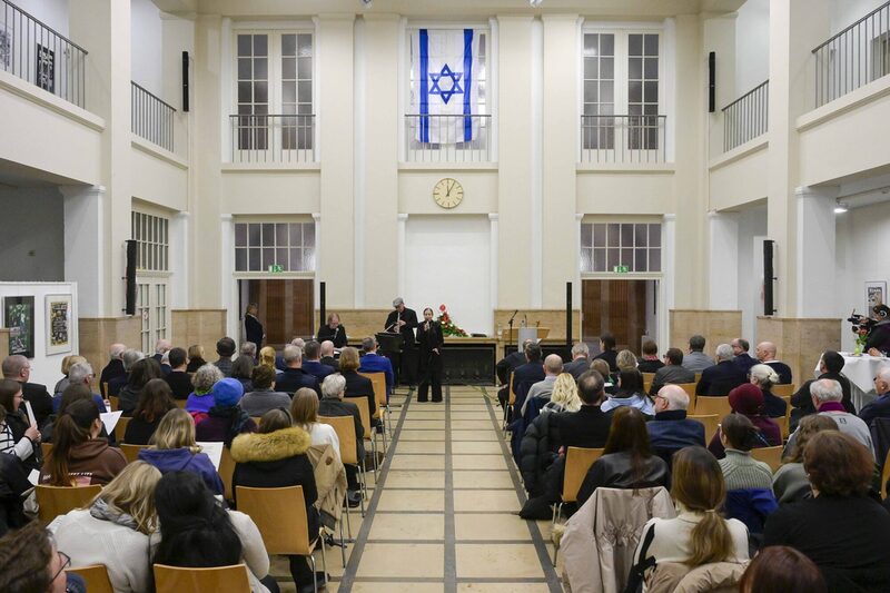 Blick auf die vollen Stuhlreihen im Lichthof, ganz vorn die drei Musiker unter einer Israel-Flagge