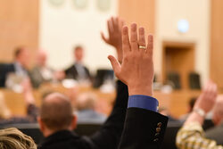 Ein Ratsmandant hebt die Hand bei einer Wahl im Ratssaal.