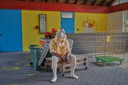 zu sehen ist ein Mann in einem Kostüm, der auf gestapelten Paletten sitzt