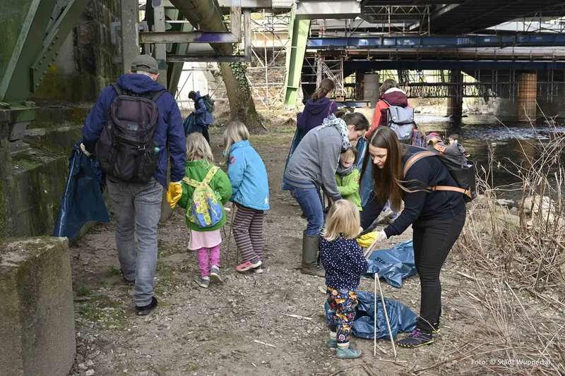 Familien sind mit Müllsäcken, Handschuhen und Greifzangen am Wupperufer unterwegs
