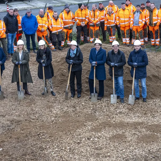 Spatenstich am Giebel mit vielen Mitarbeiterinnen und Mitarbeitern in ihren orangefarbenen Arbeitsjacken