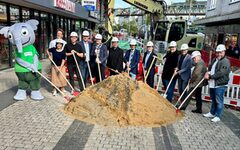 Die am Projekt Beteiligten halten Schaufeln in den Händen, die sie in Richtung eines Sandhaufens halten.