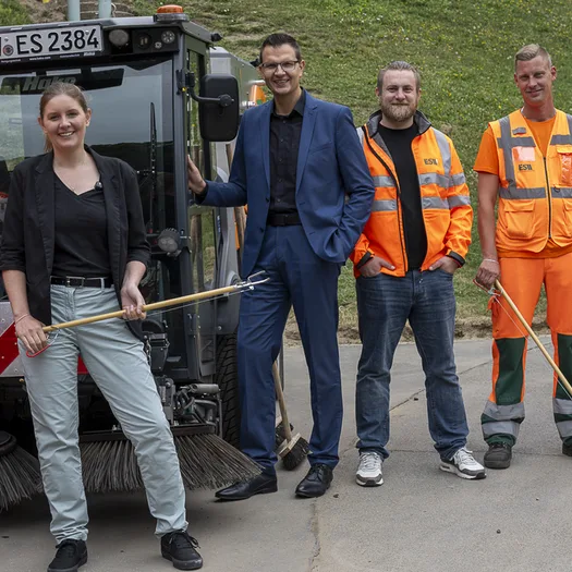 Oberbürgermeisterin Miriam Scherff, ESW-Betriebsleiter und AWG-Geschäftsführer Sascha Grabowski und Annette Berendes, Leiterin des Städtischen Ressorts Grünflächen und Forsten, mit Kollegen in Orange vor einem Elektro-Kehrfahrzeug