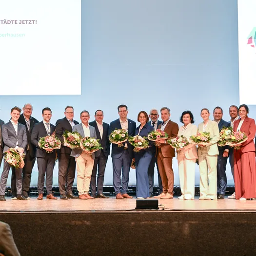 Gruppenbild des neu gewählten NRW-Städtetagsvorstandes mit Wuppertals OB Miriam Scherff - Personen auf einer Bühne mit Städtetagslogos im Hintergrund