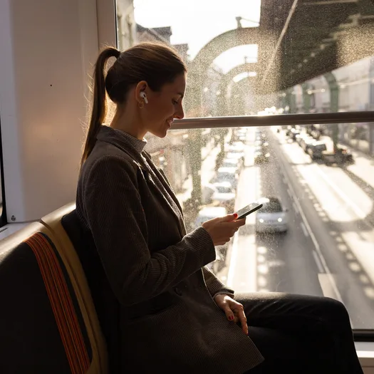 Eine Frau sitzt in der Schwebebahn und schaut auf ihr Smartphone.