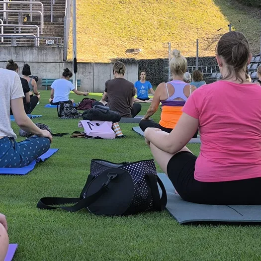Viele Menschen sitzen im Stadion am Zoo auf dem Rasen und machen Yoga.