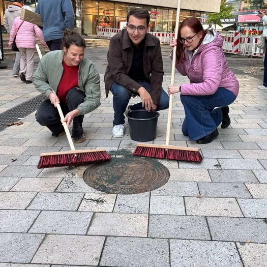 Corinna Joppien vom Innenstadtmanagement Elberfeld, Bezirksbürgermeister Sofian Goudi und Astrid Ißleib, Innenstadtkoordinatorin der Stadt Wuppertal beim verfugen der letzten Bronzetafel.