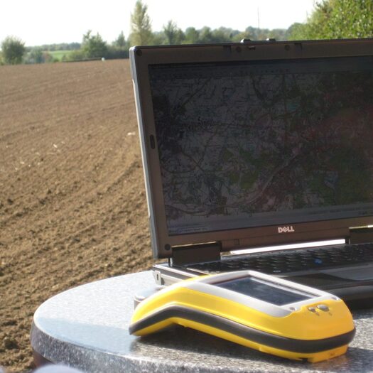Ein GPS-Empfänger und ein Laptop stehen auf einem Tisch auf einem Feld.
