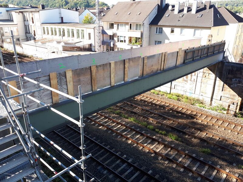 Seitenansicht Stahlbrücke über Gleisen mit Holzschutz und Gerüstturm in linker Bildecke