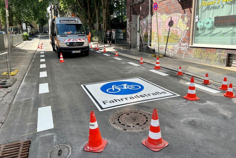 Straße mit markiertem Piktogramm Fahrradstraße, Absperrhütchen und Transporter